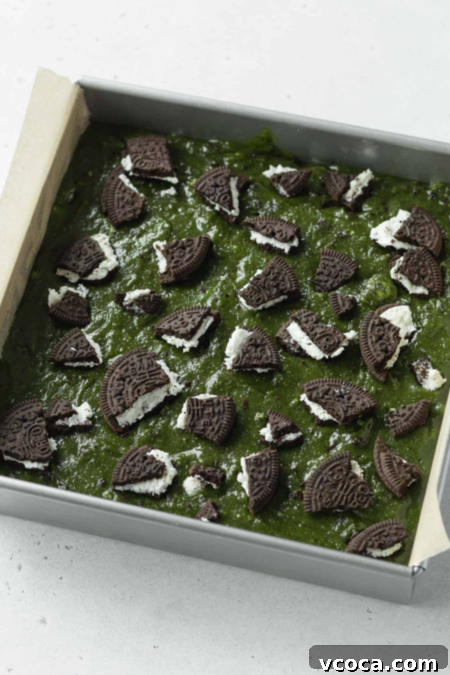 Delectable Matcha Oreo Blondies 7 Crushed Oreos sprinkled on top of green blondie batter in a pan