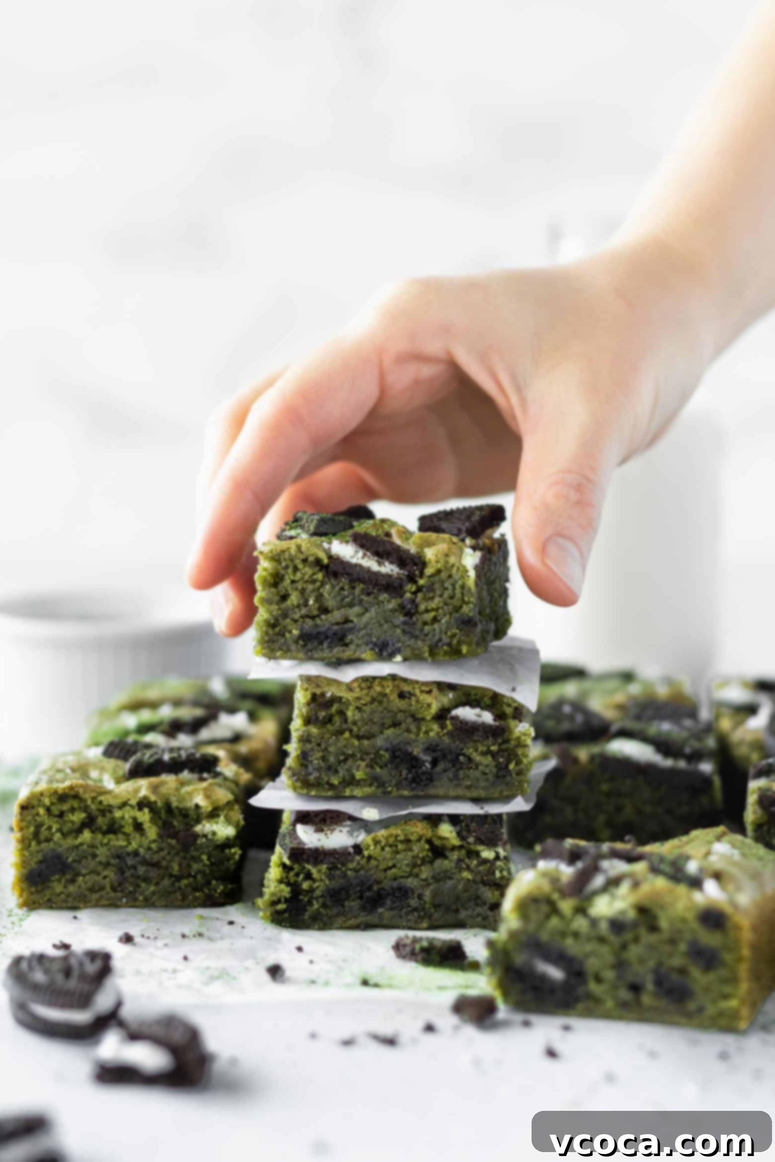 Delectable Matcha Oreo Blondies 10 A hand reaching for a stack of matcha blondies, highlighting their perfect texture and vibrant color