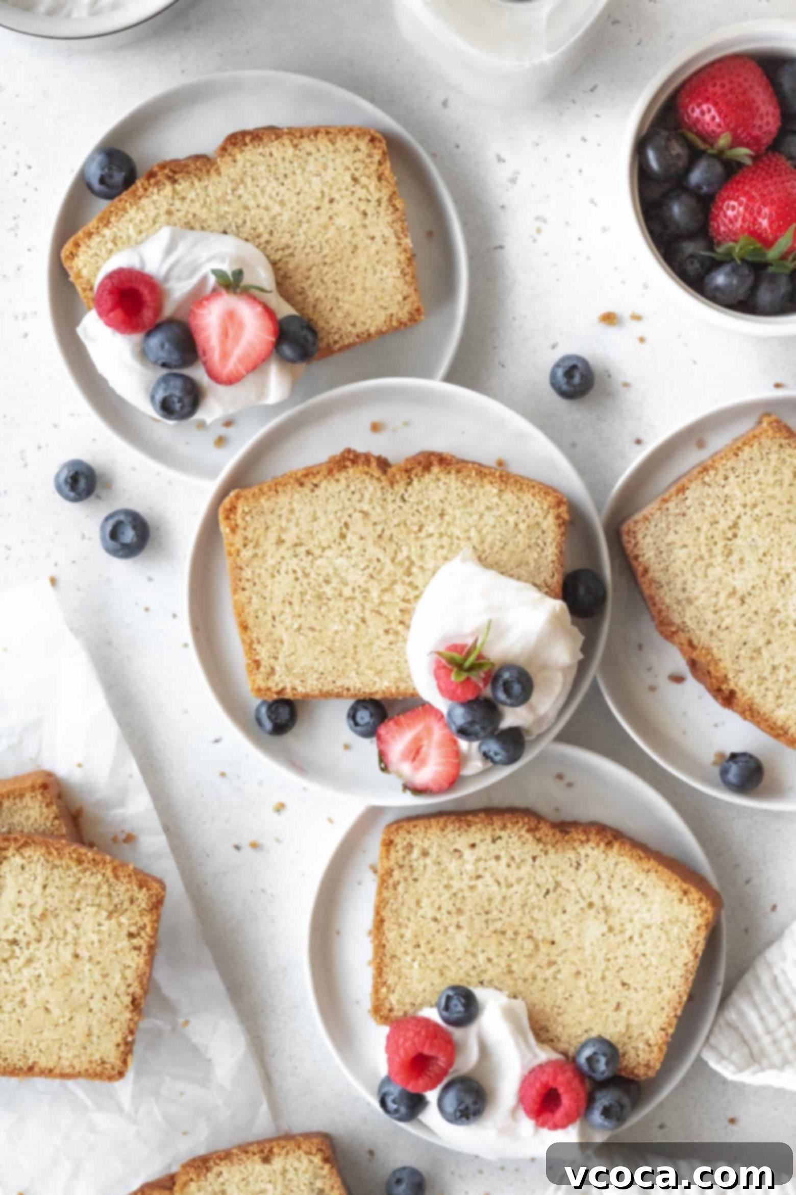 Indulgent Gluten-Free Pound Cake 4 Delicate slices of gluten-free pound cake presented on small white plates, adorned with coconut cream and fresh berries.