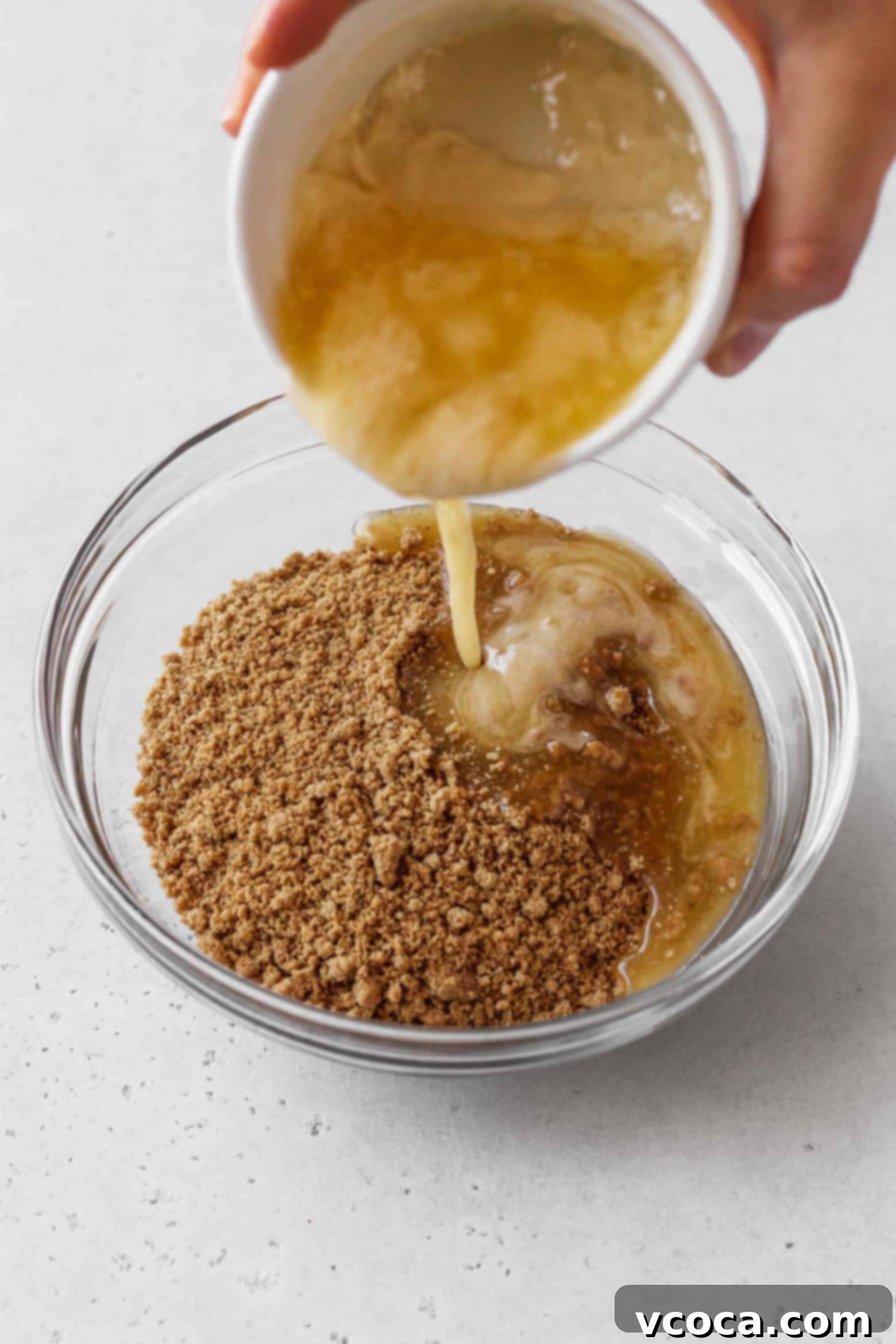 Magical Vegan Seven Layer Bars 7 Melted butter being poured into a bowl of graham cracker crumbs.