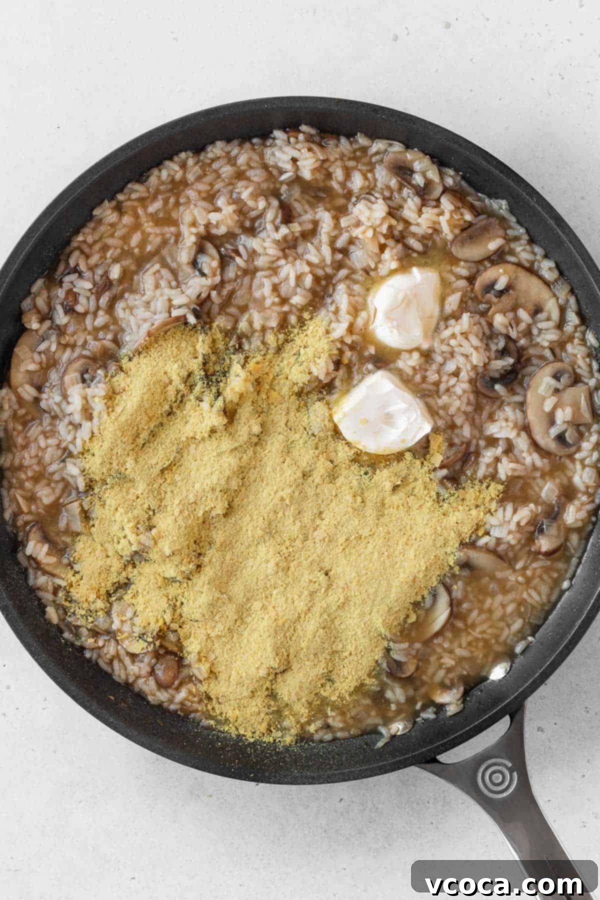 Creamy Vegan Mushroom Risotto 12 Vegan butter and nutritional yeast generously added on top of the cooked vegan mushroom risotto in the pan, ready to be stirred for creaminess.