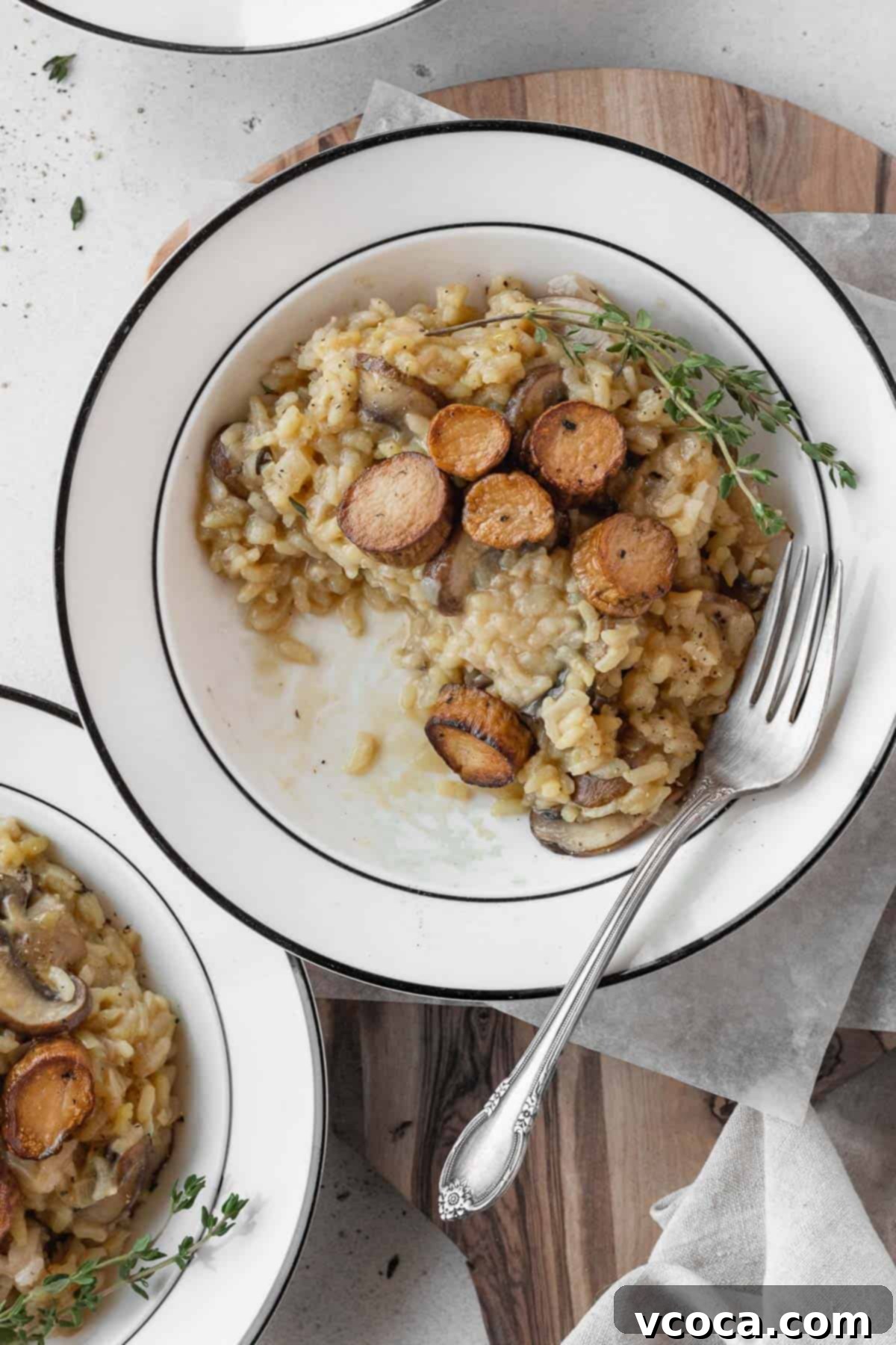 Creamy Vegan Mushroom Risotto 16 A half-eaten plate of creamy vegetarian risotto, garnished with fresh herbs and topped with seared vegan scallops, on a white tablecloth.