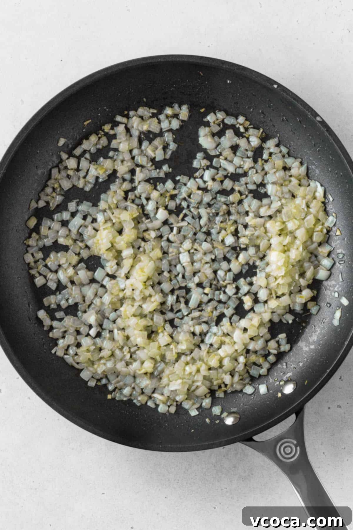 Creamy Vegan Mushroom Risotto 5 Finely chopped onions sautéing in olive oil in a black pan, starting to turn translucent.