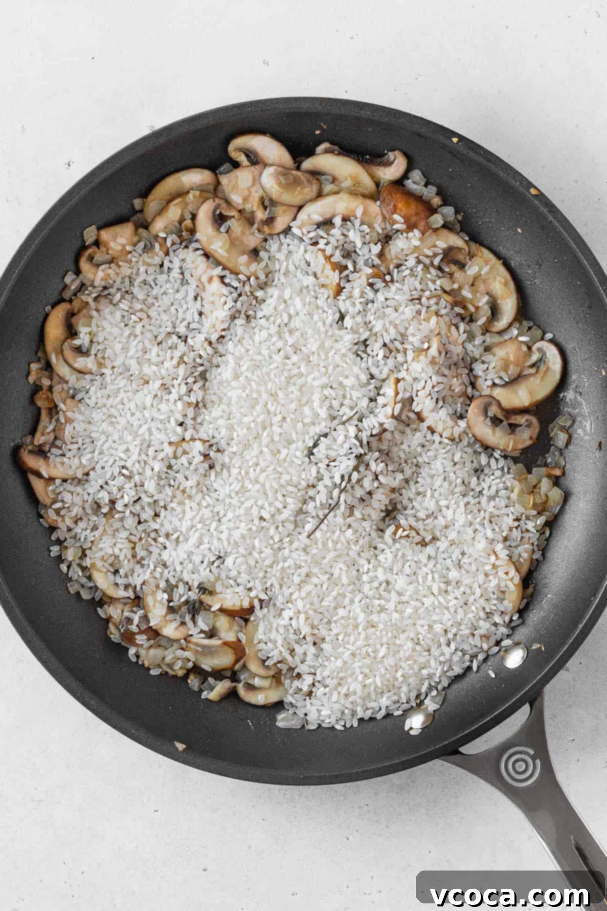 Creamy Vegan Mushroom Risotto 7 Dry Arborio risotto rice added to the pan with sautéed onions and mushrooms, ready for toasting.