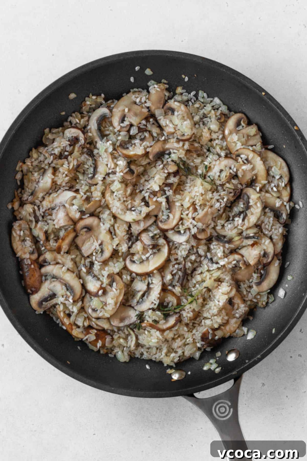 Creamy Vegan Mushroom Risotto 8 The risotto rice, onions, and sliced mushrooms toasted in a black pan, showing a light golden color.