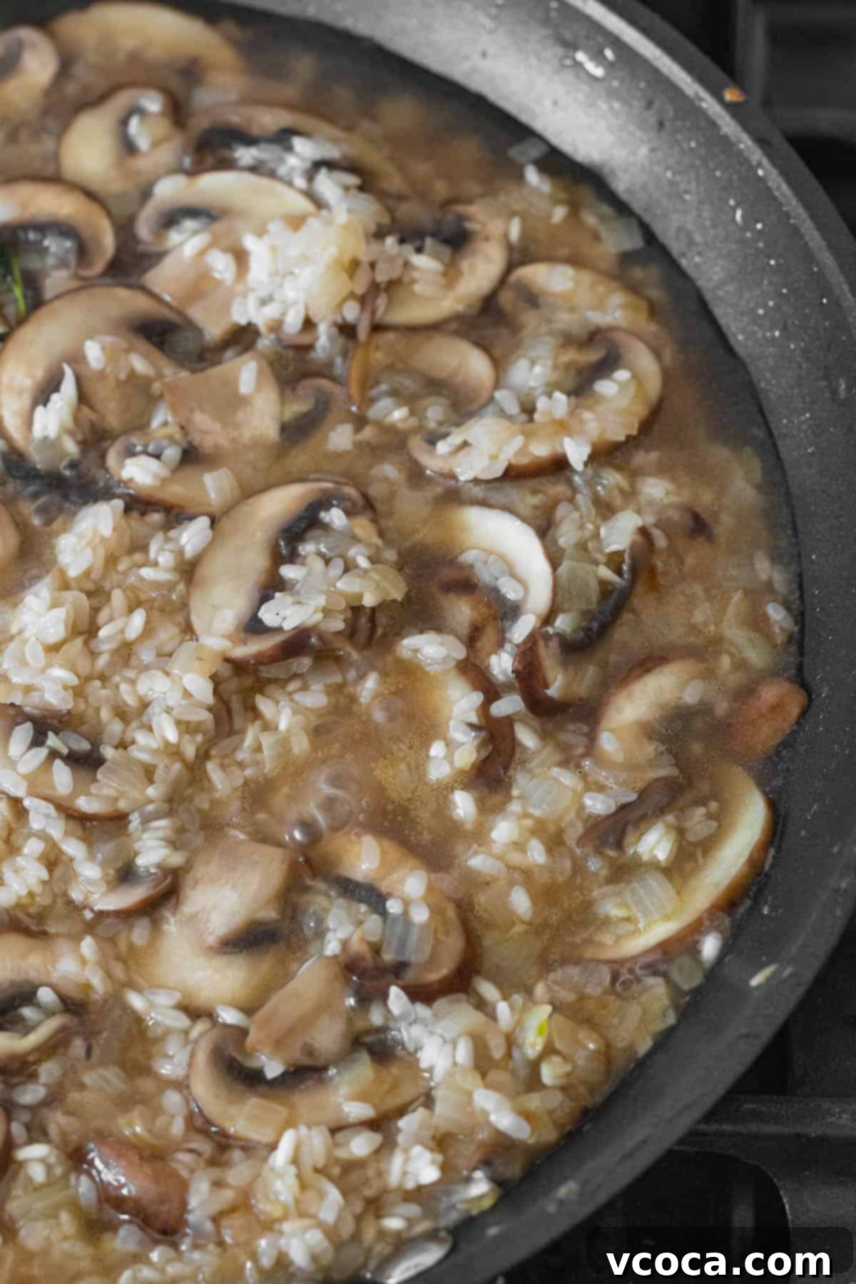 Creamy Vegan Mushroom Risotto 9 Hot vegetable stock being poured into the pan with mushroom and toasted risotto rice, ready to be stirred.