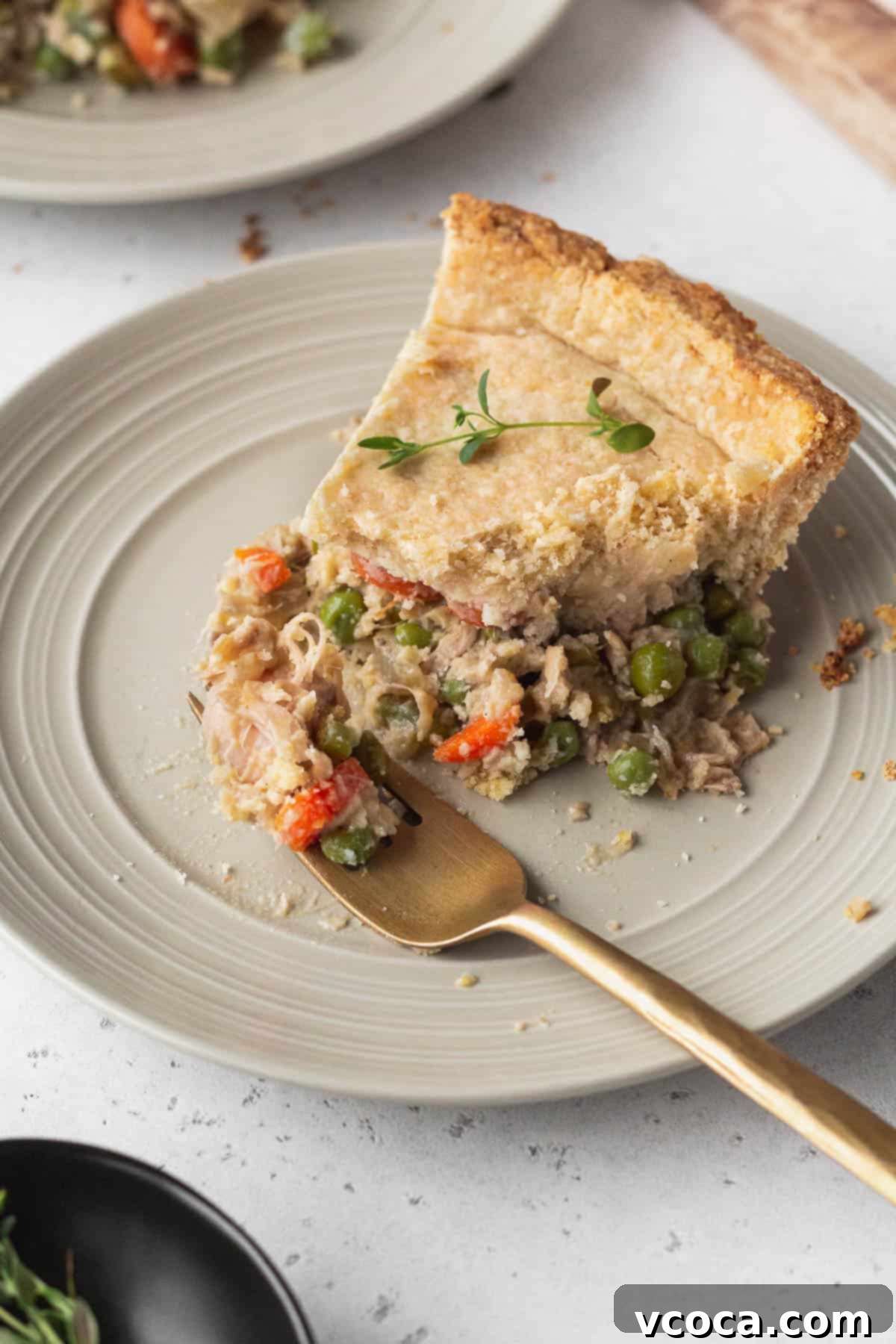 Vegan Chicken Pot Pie 2 A golden-brown slice of vegan chicken pot pie on a white plate, with a fork taking a bite, showing the creamy filling and vegetables.