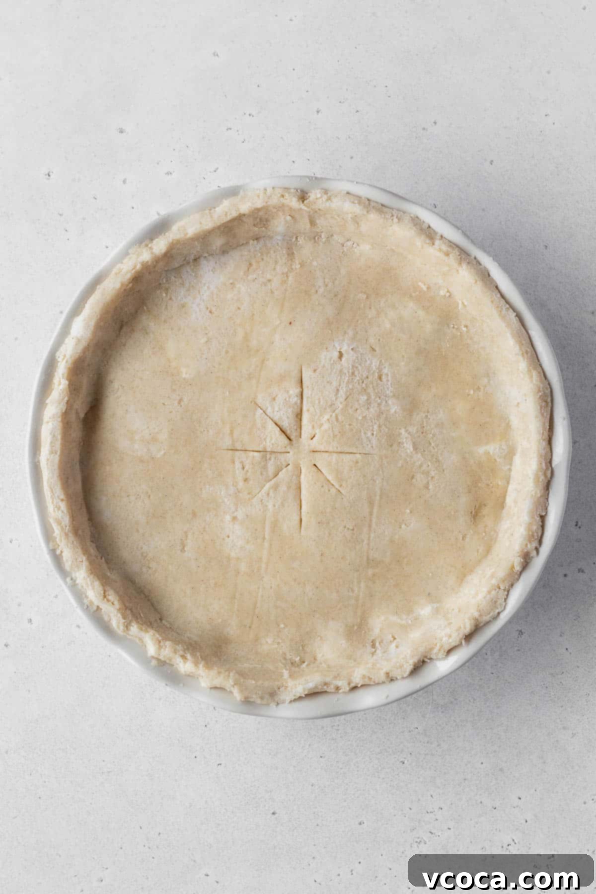 Vegan Chicken Pot Pie 12 An unbaked vegan pot pie, topped with a raw pie crust with steam vents cut into it, on a grey surface.