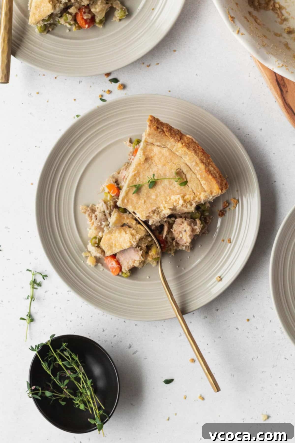 Vegan Chicken Pot Pie 15 A golden slice of vegan chicken pot pie on a white plate, with a gold fork cutting into the creamy filling, showing the rich texture.