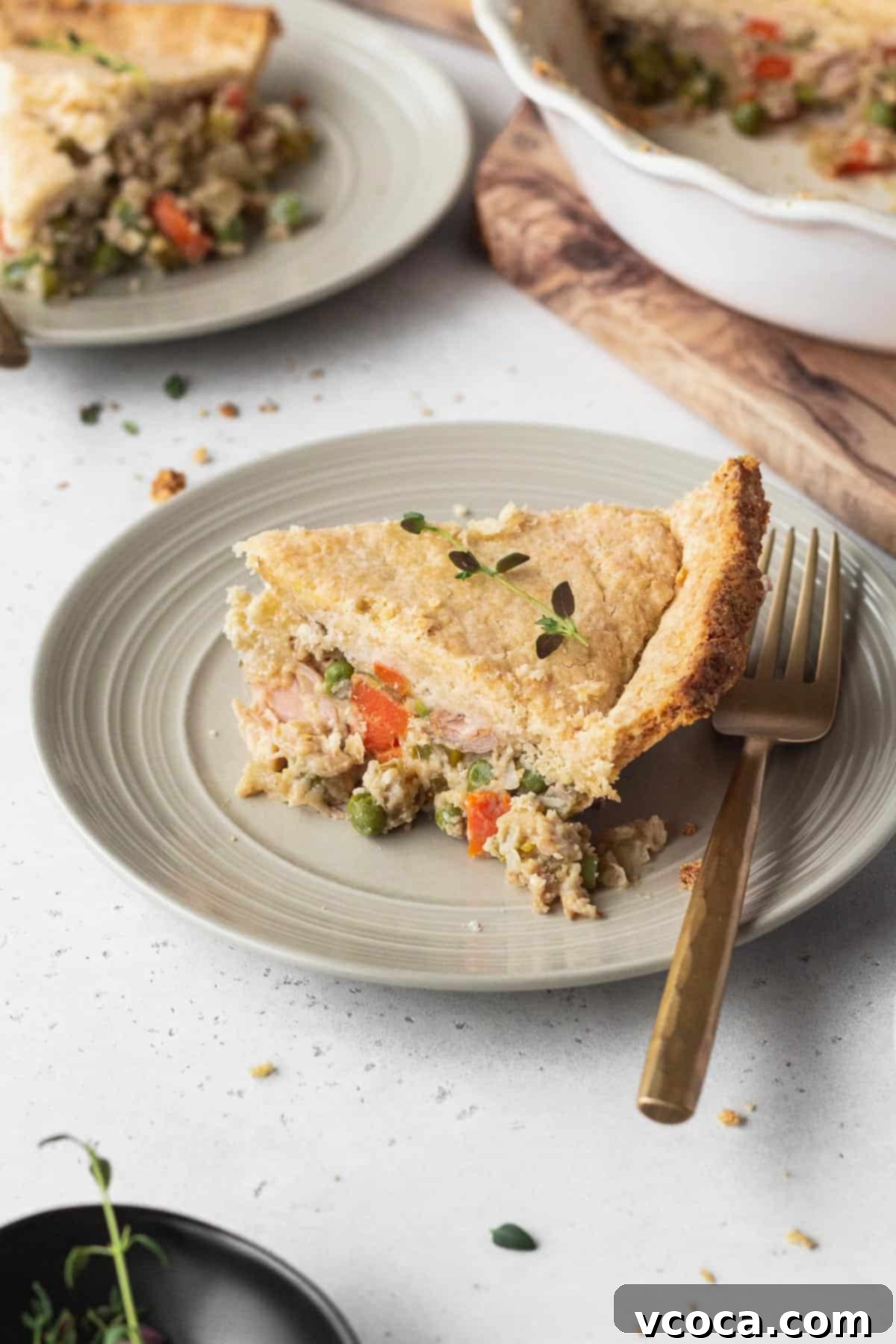 Vegan Chicken Pot Pie 3 A perfectly baked slice of vegan pot pie on a white plate with a gold fork, showcasing the flaky crust and rich filling.